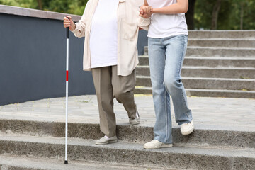 Young woman with blind grandmother walking on stairs in park