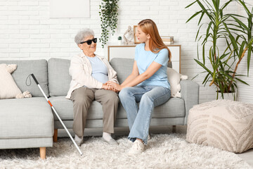 Young woman with blind grandmother sitting on sofa at home