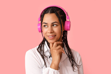 Young African-American woman listening to music on pink background