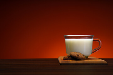 The chocolate chip cookie biscuit with a cup of milk on a orange background. 
