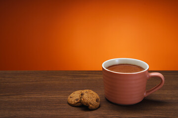 The chocolate chip cookie biscuit with a cup of chocolate drink on a orange background. 