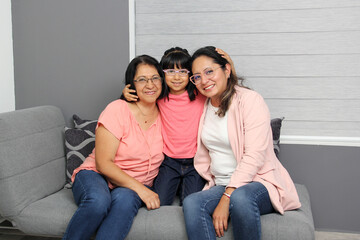 Three generations of brunette Latina women: grandmother, mom and daughter with glasses show their love and celebrate Mother's Day