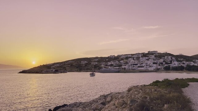 Golden hues fill the sky as the sun sets over Donousa, highlighting the serene village and gentle waves lapping at the shoreline.