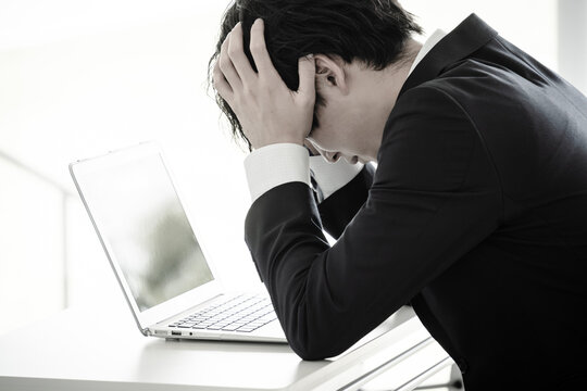 デスクで頭を抱えながら悩む若い男性ビジネスマン
