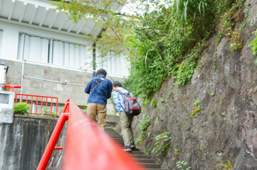 赤い手すりが設置されている階段を上る男性の後ろ姿