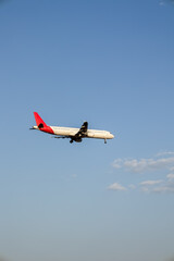 Vertical photograph of a white and red plane landing on a clear sky with some clouds at sunset.