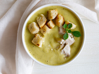 bowl of homemade zucchini cream soup with chicken and basil with croutons on white wooden table. Top view flat lay, close up
