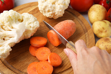 Cooking vegetable stew. Woman cutting carrot at table, closeup