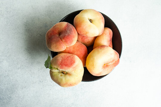 Overhead view of a bowl of ripe flat peaches on a table