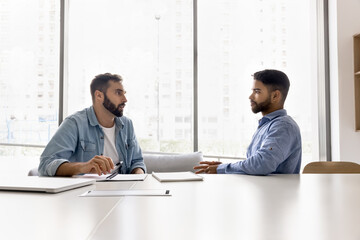 Serious young multiethnic male business partners meeting at large white table for negotiation,...