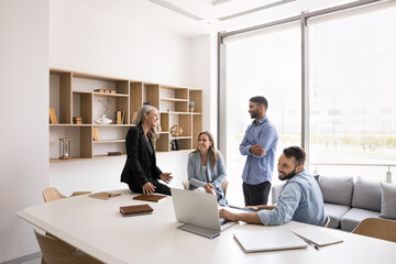 Happy diverse business team meeting in white colored modern office interior, sitting, standing at...