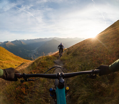 Personal perspective view of a man following a woman mountain biking at sunset, Gastein Valley, Salzburg, Austria