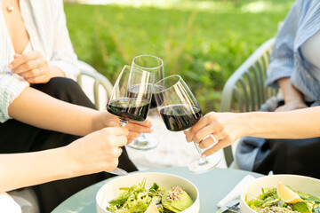 Close-up of three women having lunch outdoors making a celebratory toast with glasses of red wine