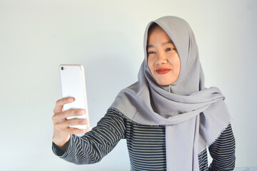 Portrait of an Asian woman holding a smartphone while smiling at the camera and raising her hand showing an okay gesture. on an isolated background