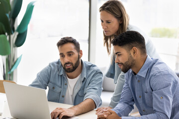 Small diverse business team meeting at office, watching online content on pc, using computer for teamwork, cooperation, working together, App developer showing slide presentation to colleagues
