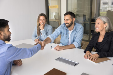 Fototapeta premium Two cheerful diverse business partners men ending successful talk, discussing acquisition, cooperation, shaking hands at board meeting, getting agreement, smiling, laughing