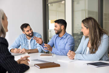 Obraz premium Cheerful young Arab business professional man talking to diverse colleagues at meeting, telling creative ideas, brainstorming on cooperation, discussing teamwork, smiling, laughing