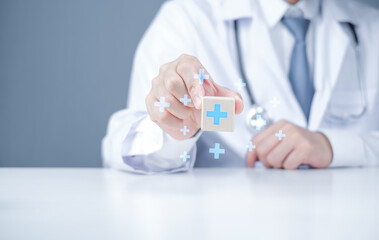 Obraz premium Doctor holding wooden block with medical cross symbol. Studio shot with blurred background. Healthcare and medical services concept for banner and poster