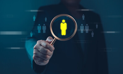 Hand holding magnifying glass Recruitment and human resources concept highlighting yellow figure among blue figures. Studio shot with blurred person in background. for banner and poster