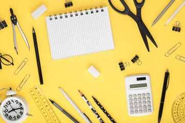 Stationery in black and white, notebook, alarm clock and calculator on a yellow background. Back to...