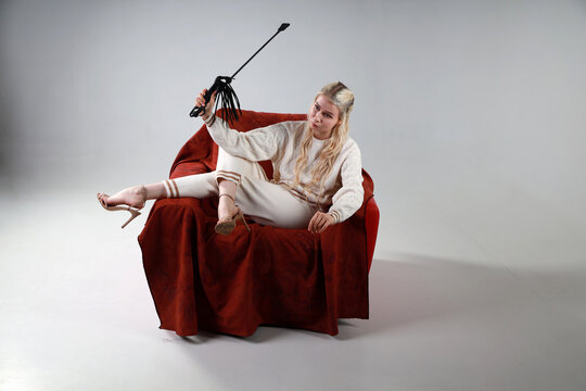 Pretty blonde woman with whip sitting in red armchair