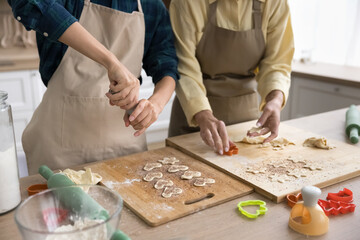 Hands of two younger and older baker women in kitchen aprons cutting fresh dough for cookies on table, baking heart and star shaped biscuits together, preparing homemade sweet