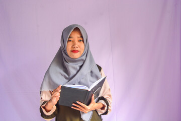 Portrait of joyful smiling positive woman with dark wavy hair standing holding paper notebook and showing empty paper, copy space. Indoor studio shot isolated on background.