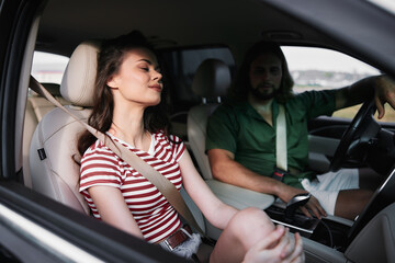 Young couple sitting in a car, enjoying a moment together, with the woman relaxed and the man attentive The background depicts a scenic landscape