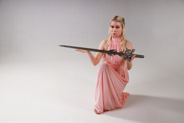 Beautiful blonde woman in pink dress holding a sword