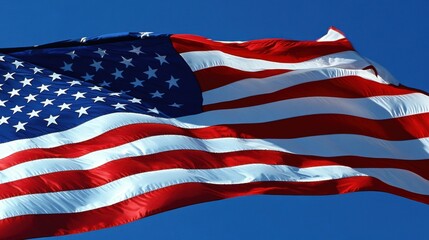 Fototapeta premium A close-up of an American flag waving in the wind against a clear blue sky, the stars and stripes clearly visible, symbolizing patriotism and freedom, evoking a sense of pride and national identity,