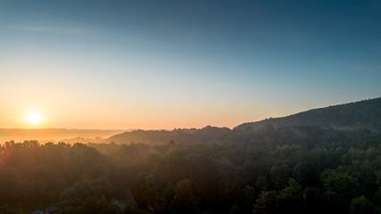 Sunrise casting golden light over misty forest hills in early morning