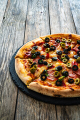 Circle pizza chorizo with black and green olives slices and mozzarella served on black stony plate on wooden table
