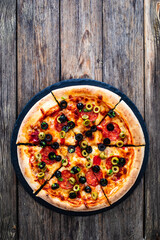 Circle pizza chorizo with black and green olives slices and mozzarella served on black stony plate on wooden table
