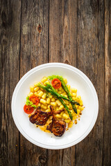 Lamb chops with bone, gnocchi and cooked green asparagus served on white plate on wooden table
