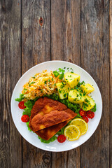 Crispy breaded fried pork chop, boiled potatoes and sauerkraut salad served on white plate on wooden table
