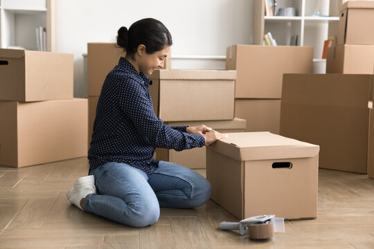 Small business owner working in warehouse, prepare parcel for dispatch to client use reliable transportation services. Happy Indian woman packing personal belonging, Moving, relocation, drop shipping