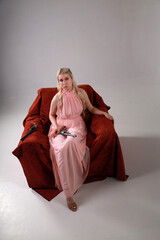 Pretty blonde woman in pink dress with two revolvers sitting in a red armchair