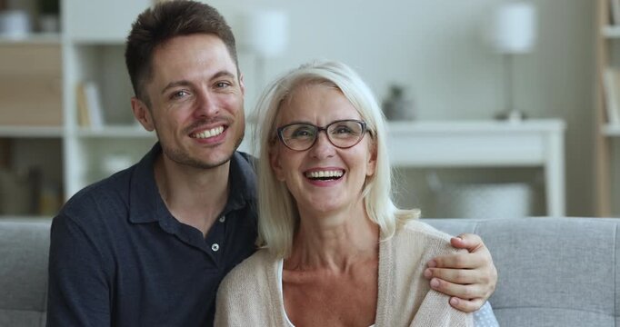 Happy loving adult son embracing cheerful mom with care, support, affection, looking at camera with toothy smile, laughing, closing eyes, enjoying family relations, good relationship