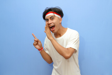 Indonesian man in white shirt and Indonesian flag doing whisper while pointing finger  to the side with happy excited face,Indonesian independence day concept