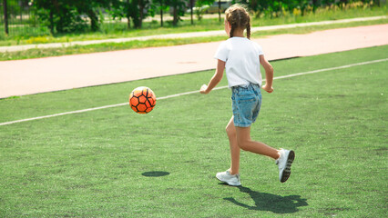 childhood, leisure games and people concept - happy little girl with ball playing soccer at school field