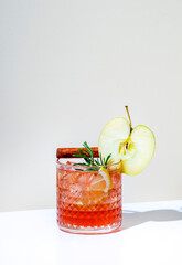 Red apple cocktail drink with vodka, liqueur, cinnamon, lemon with rosemary on beige background,...