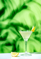 Alcoholic cocktail drink with gin, vodka, aperitif, lemon zest and ice in glass on green background, hard light