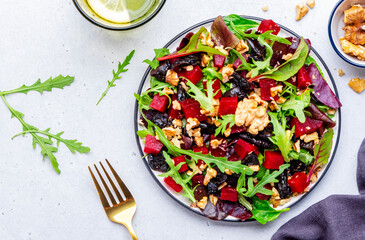 Fresh crispy vegan salad with baked beetroot, dried prunes, arugula, chard and lnuts, white background