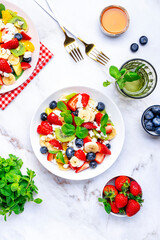 Fruit summer salad with berries, ricotta cheese, mint and honey, white marble background, top view