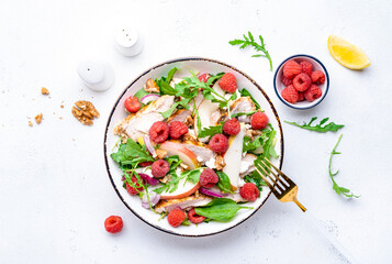 Delicious summer salad with raspberries, chicken meat, fresh pears, ricotta cheese, red onion, nuts, spinach and arugula, white background, top view