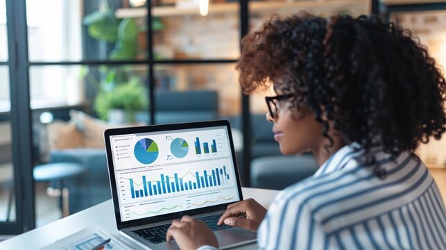 Black woman examining financial information on computer display in blended office environment for online business performance indicator control panel.