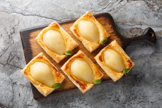 Pears poached in sweet vanilla cinnamon liquid and baked in puff pastry closeup on the wooden board on the table. Horizontal top view from above - Powered by Adobe