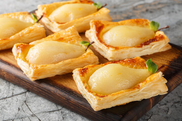 Caramelized pears baked in puff pastry and stuffed with nuts and cream cheese close-up on a wooden board. Horizontal