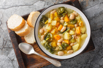 Vegetable soup with beans, potatoes, pumpkin, kale, carrots, onions and celery close-up in a bowl on the table. Horizontal top view from above