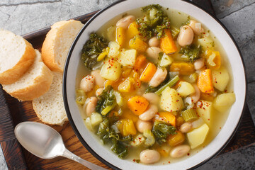Italian Bean and Vegetable Soup Zuppa alla Frantoiana closeup on the bowl on the wooden board. Horizontal top view from above
